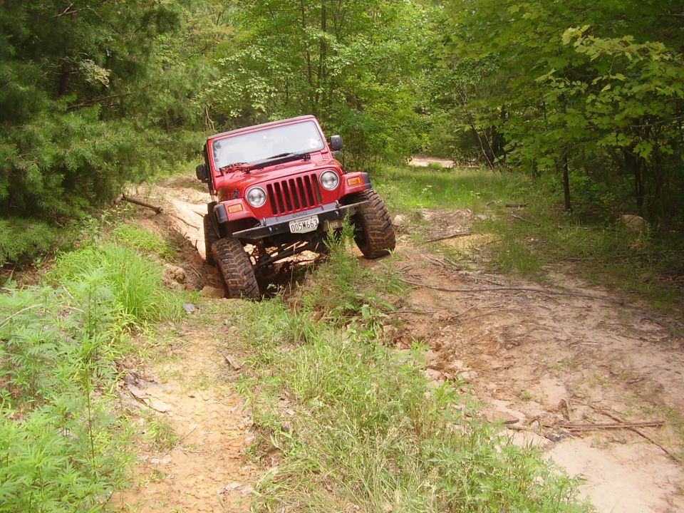 Red Jeep Wrangler navigating a muddy off-road trail with tall tires