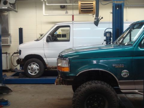 1996 Ford Bronco - A 1996 Ford Bronco and a white Ford Econoline van are parked on lifts inside a workshop.