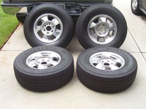 2004 Chevrolet Silverado 1500 - Four aftermarket tires and rims are displayed on a concrete surface, with the rear bumper of a truck visible in the background.