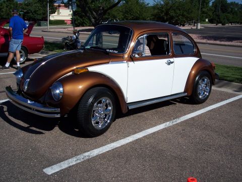 1972 Ford Ranchero - A two-tone brown and white Volkswagen Beetle is parked in a lot, its chrome wheels and classic design.