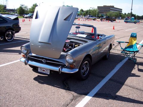1972 Ford Ranchero - A silver convertible sports car is parked with its hood open, next to a folding chair in a parking lot.
