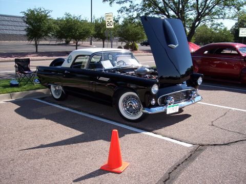 1972 Ford Ranchero - A black 1957 Ford Thunderbird with its hood open is parked next to a red car at an outdoor event.