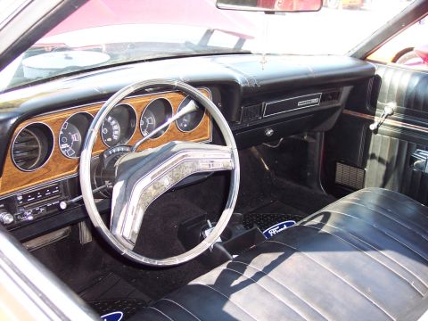 1972 Ford Ranchero - The interior of a 1972 Ford Ranchero features a woodgrain dashboard, black vinyl seats, and a prominent steering wheel.