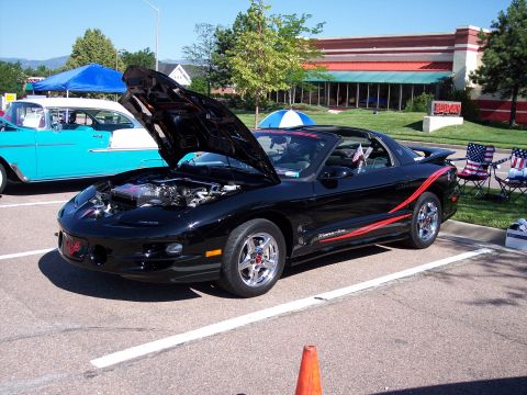 1972 Ford Ranchero - A black 1998 Pontiac Firebird Trans Am is displayed with its hood open, parked beside a vintage turquoise car at a show.