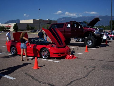 1972 Ford Ranchero - Two vehicles, a red convertible and a lifted pickup truck, are displayed with their hoods open at a car show.