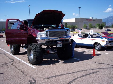 1972 Ford Ranchero - A lifted pickup truck with its hood open is parked next to a classic muscle car.