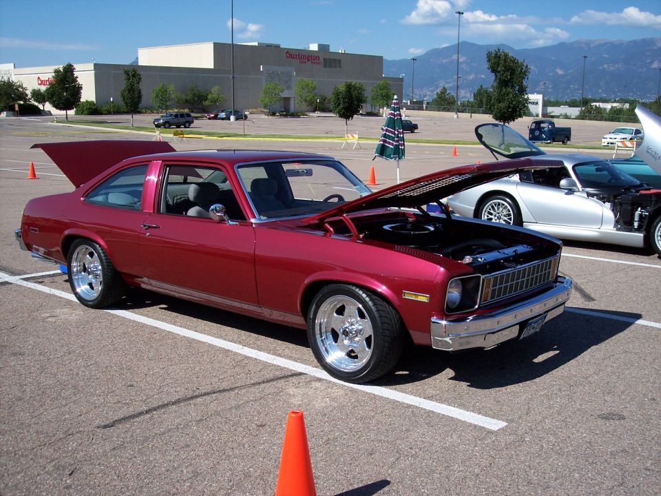 Red 1975 Chevrolet Nova coupe with hood and trunk open, parked next to a silver sports car
