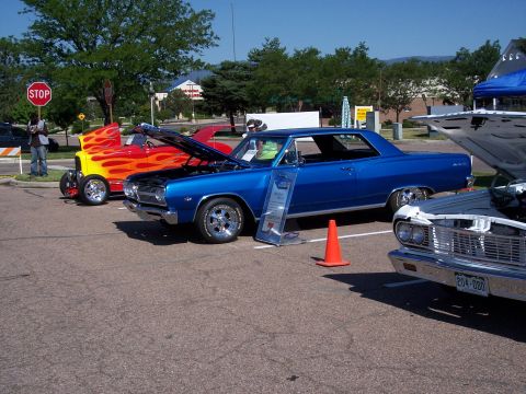 1972 Ford Ranchero - A blue coupe and a flame-painted hot rod are displayed at an outdoor car show.