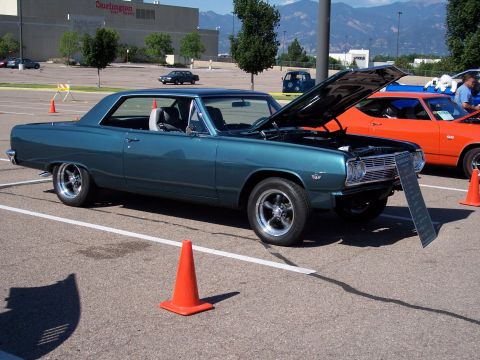 1972 Ford Ranchero - A teal 1965 Chevrolet Chevelle coupe is displayed with its hood open at a car show.