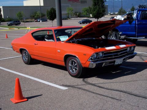 1972 Ford Ranchero - Orange 1969 Chevrolet Chevelle SS parked at an outdoor event, hood open, with a blue pickup truck in the background.