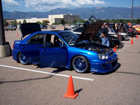 1972 Ford Ranchero - A bright blue Subaru WRX STI is displayed with its hood and doors open, custom modifications at an outdoor event.