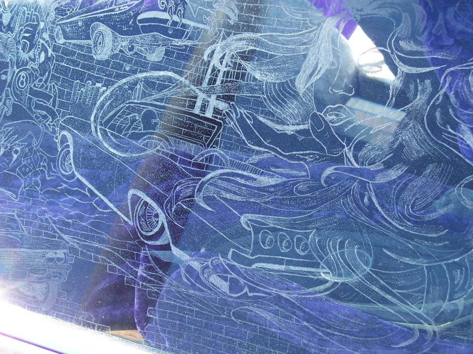 Etched glass art on a vehicle window shows a classic car and a woman's face
