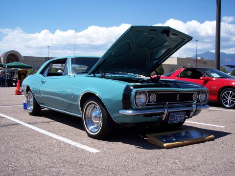 1972 Ford Ranchero - Teal 1967 Chevrolet Camaro at a car show, hood up, with a red car nearby.