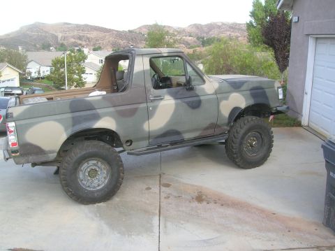 1985 Ford Bronco - Side view of a camouflaged Ford Bronco with lifted suspension and off-road tires.