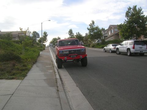 1985 Ford Bronco - A red Ford truck is parked on the side of a street in a residential area.