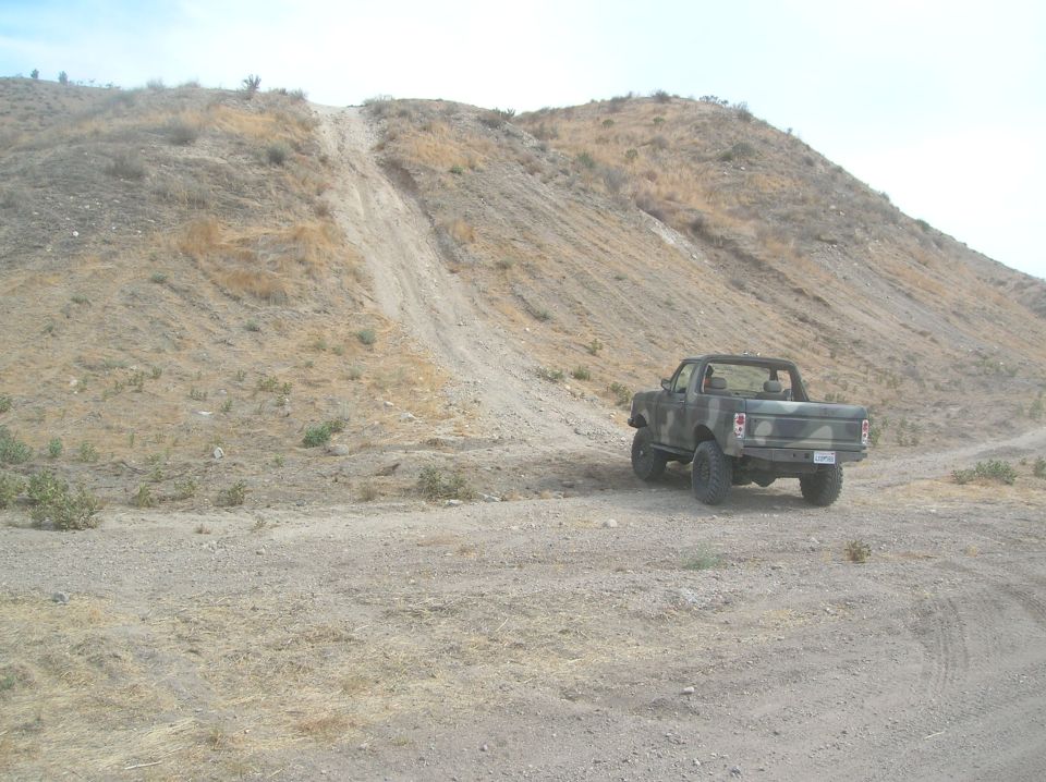 Camouflage truck from rear, parked on dirt road with hill in background