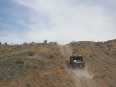 1985 Ford Bronco - Pickup truck navigates a dusty, off-road trail on a cloudy day.