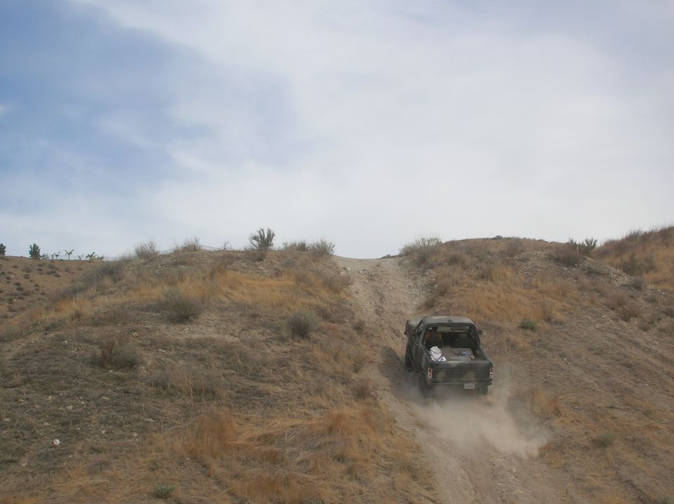 Camouflaged pickup truck kicking up dust as it drives up a steep dirt hill