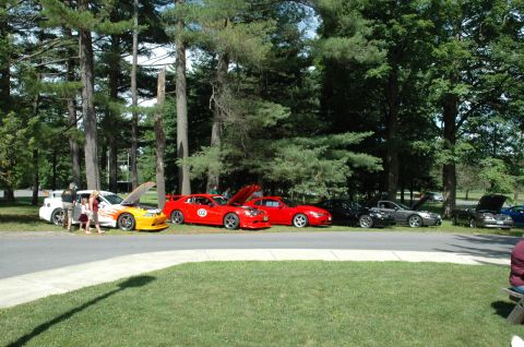 2000 Ford Mustang - A row of cars are parked on the side of the road, with people milling around them.
