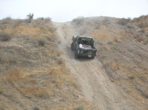 1985 Ford Bronco - Pickup truck navigates a steep, dry, dirt hill, kicking up dust.