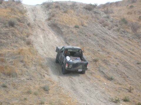 1985 Ford Bronco - A camouflaged pickup truck navigates a steep, dry, dirt path on a hillside.