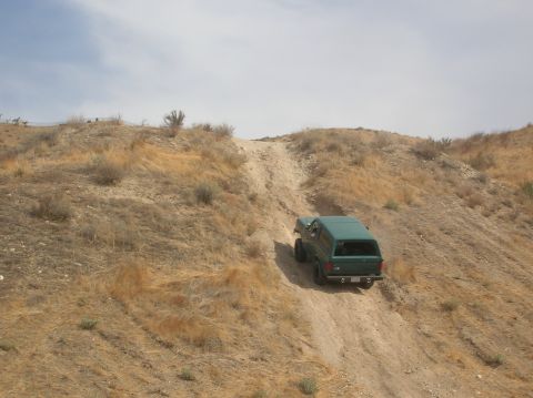 1985 Ford Bronco - Green 1985 Ford Bronco navigates a challenging off-road trail on a dry, sunny day.