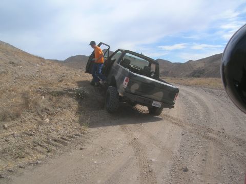 1985 Ford Bronco - A camouflaged 1985 Ford Bronco is seen on a dirt road with a person exiting the driver's side door.