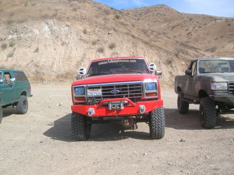 1985 Ford Bronco - This red Ford Bronco features a custom front bumper with a winch, and a website sticker on the windshield.