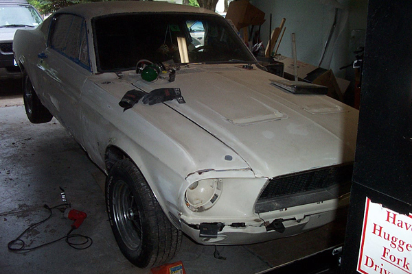 White 1967 Ford Mustang undergoing restoration, front quarter view, primer finish, missing headlight bezel