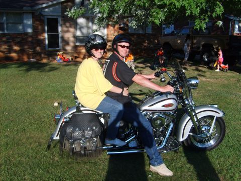 1999 Harley-Davidson Softail - A couple rides a silver motorcycle on a sunny day, with a house and truck in the background.