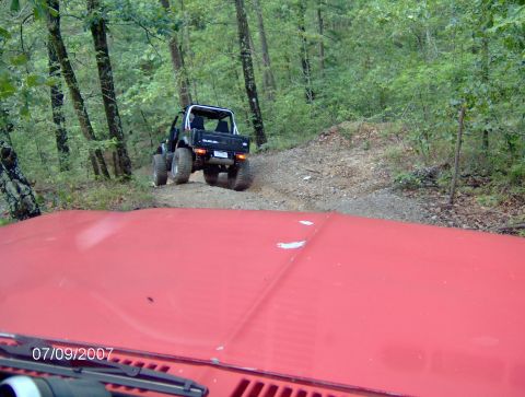 1978 Ford Bronco - A black Suzuki Samurai navigates a wooded trail, with the hood of another vehicle visible in the foreground.