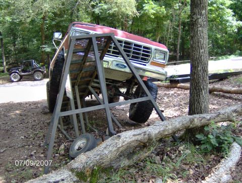 1978 Ford Bronco - A red Ford truck is positioned on a metal ramp, with another off-road vehicle visible in the background.