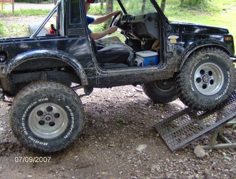 1978 Ford Bronco - A black off-road vehicle is shown from a 3/4 front angle as it ascends a metal ramp.