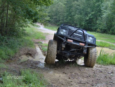 1978 Ford Bronco - Suzuki Samurai navigates a muddy off-road trail with water obstacles.