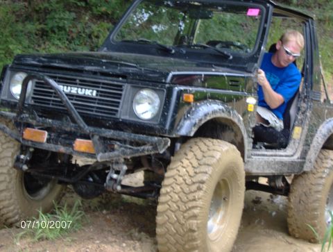 1978 Ford Bronco - A man drives a muddy Suzuki Samurai on a dirt trail.