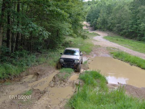 1978 Ford Bronco - A pickup truck navigates a muddy off-road trail surrounded by trees.