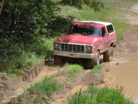 1978 Ford Bronco - Red 1978 Ford Bronco navigates a muddy trail on a sunny day.