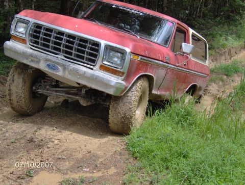 1978 Ford Bronco - A red 1978 Ford Bronco navigates a challenging muddy trail, its tires caked in dirt.