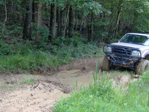 1978 Ford Bronco - Off-road vehicle navigating a muddy trail through a wooded area.