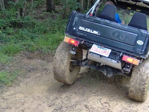 1978 Ford Bronco - A black Suzuki Samurai navigates a muddy off-road trail, showing its rear end and large tires.