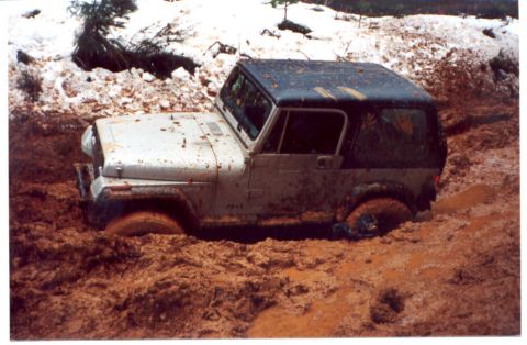 1989 Ford Bronco - This Jeep Wrangler is deeply stuck in a muddy terrain, with snow visible on the higher ground.