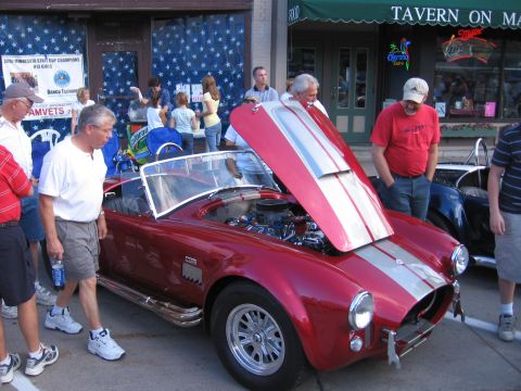 1989 Ford Mustang - Car show with a red convertible sports car and onlookers. The hood is open to reveal the engine.