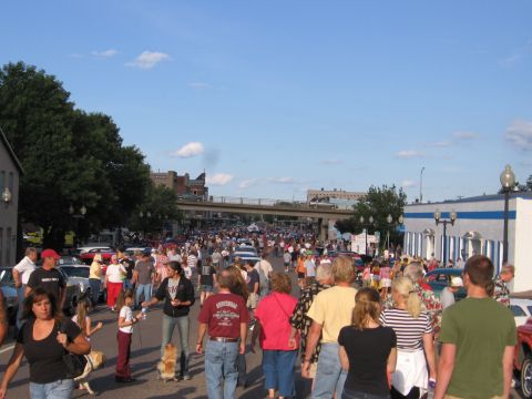 1989 Ford Mustang - A street fair is in full swing with many people walking around and cars parked along the sides.