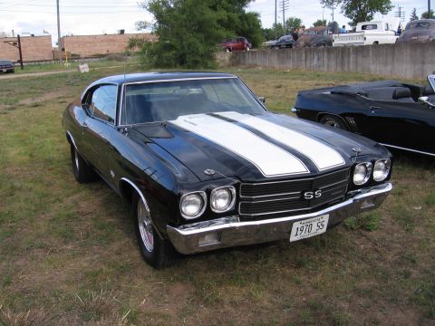 1989 Ford Mustang - A black 1970 SS muscle car with white racing stripes is parked on grass next to another car.