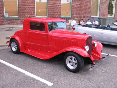1989 Ford Mustang - A red hot rod coupe is parked next to a silver convertible at a car show.