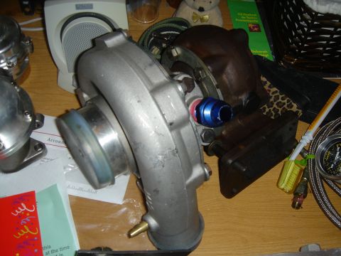 1995 Mazda MX-6 - Turbocharger and blow-off valve components are laid out on a wooden surface with other miscellaneous items.