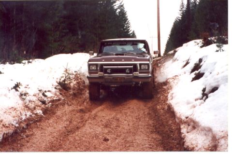 1989 Ford Bronco - This maroon Ford F-Series truck navigates a challenging muddy and snowy road, likely an off-road trail.