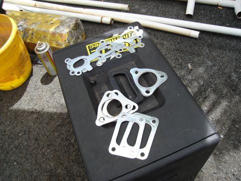 1995 Mazda MX-6 - Several exhaust manifold gaskets are laid out on a black toolbox, with a yellow bucket and spray can nearby.