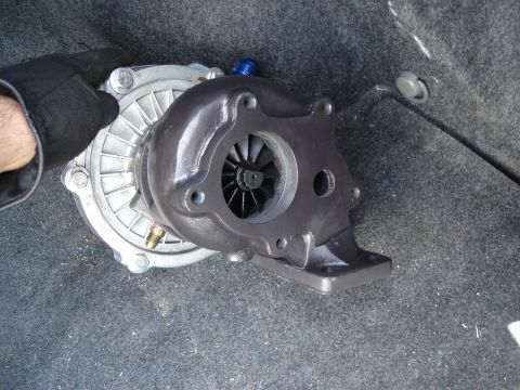 1995 Mazda MX-6 - A turbocharger is shown, likely for a performance upgrade project. The part is resting on a carpeted surface.