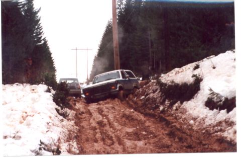 1989 Ford Bronco - Two trucks navigate a muddy, snow-covered path lined with trees and a utility pole.